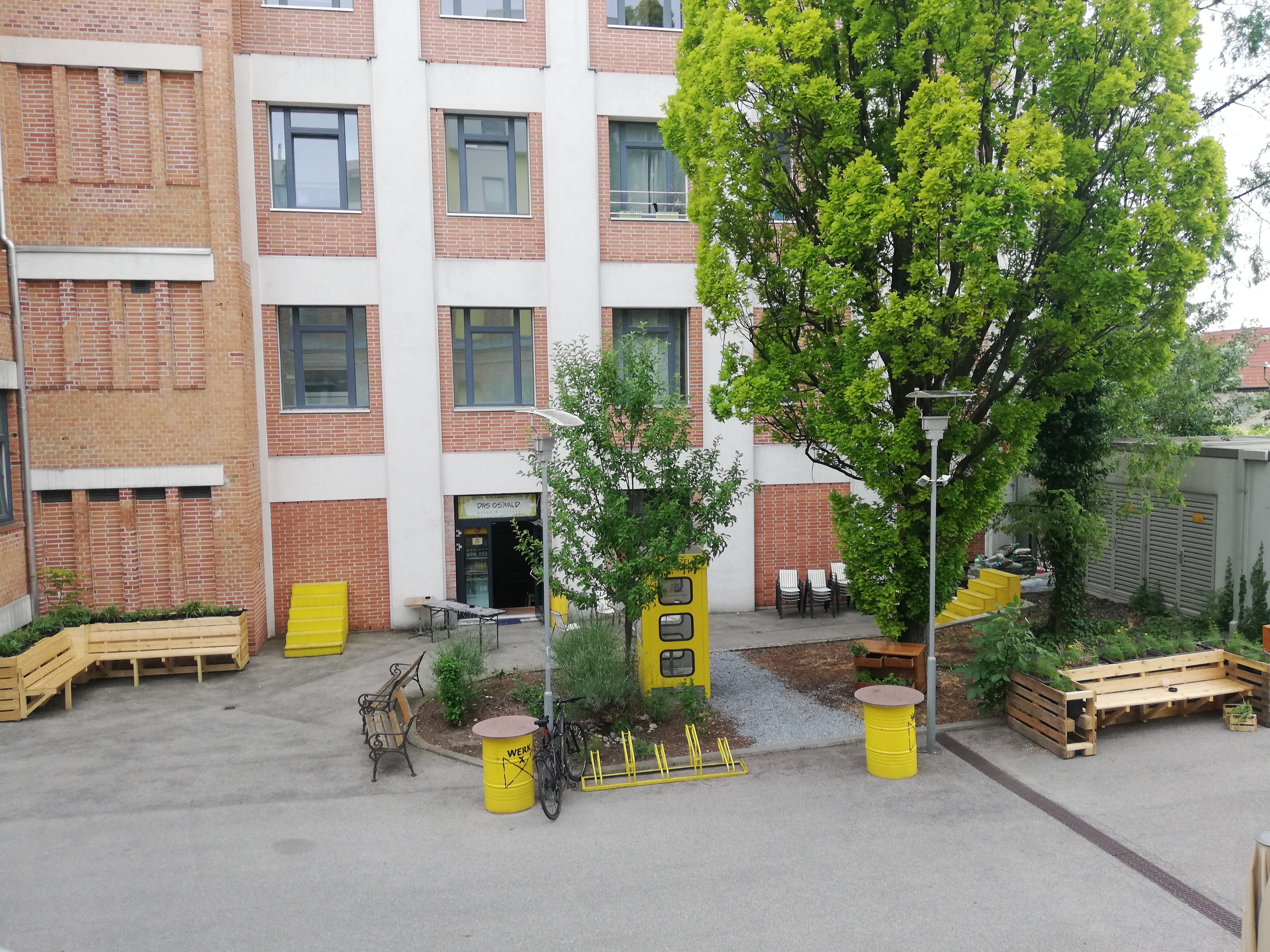 Backsteingebäude, Innenhof, bepflanzte Sitzmöbel aus Holz